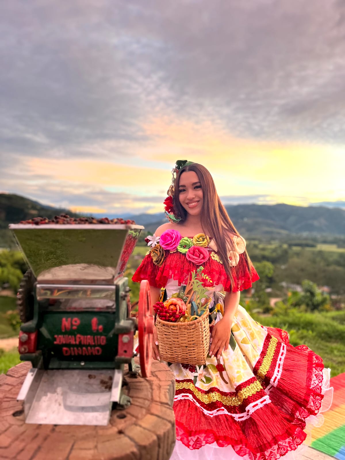 Mujer con traje típico junto a una despulpadora de café al atardecer